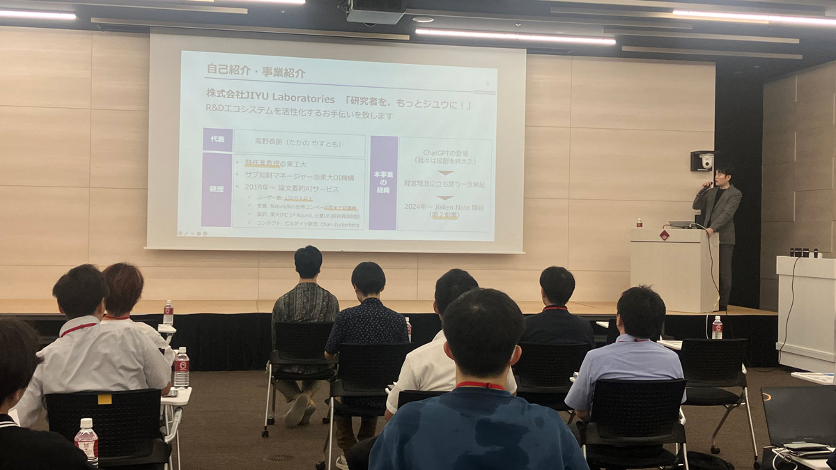 早稲田大学ナノテクノロジーフォーラムでの登壇風景。発表者が自己紹介スライドを投影し、参加者が前列で聴講している様子。